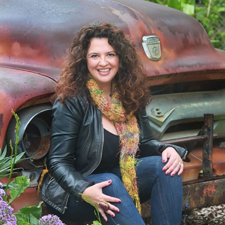 A woman sitting on the ground next to an old truck.