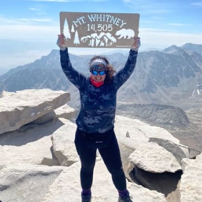 A woman holding up a sign on top of a mountain.