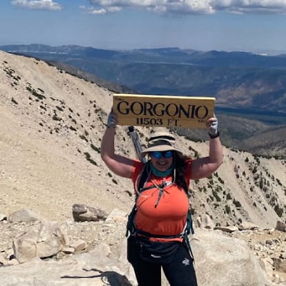 A woman holding up a sign on top of a mountain.